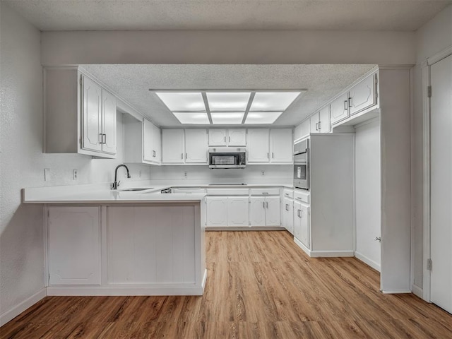 kitchen featuring kitchen peninsula, light wood-type flooring, stainless steel appliances, sink, and white cabinets