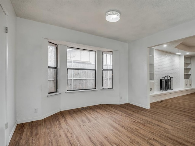 unfurnished living room with a fireplace, hardwood / wood-style floors, a textured ceiling, and built in shelves