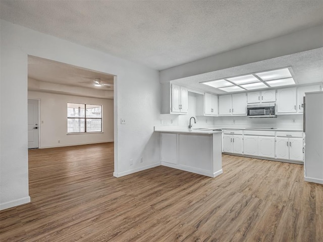 kitchen featuring kitchen peninsula, a textured ceiling, light hardwood / wood-style floors, and white cabinetry