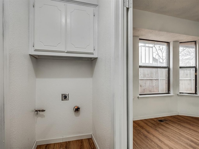 laundry area with hookup for an electric dryer, cabinets, and light wood-type flooring