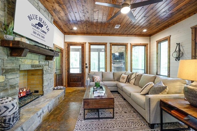 living room with ceiling fan, a stone fireplace, wooden ceiling, and wooden walls