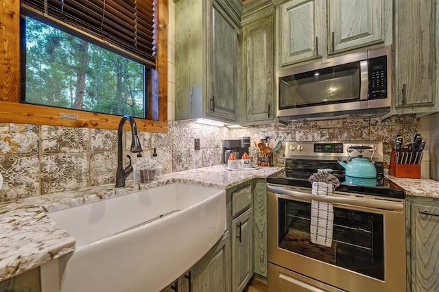 kitchen with decorative backsplash, appliances with stainless steel finishes, light stone counters, sink, and green cabinetry