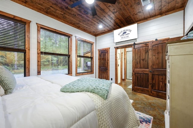 bedroom featuring a barn door, wooden ceiling, ceiling fan, and wooden walls