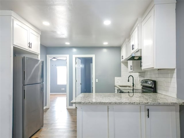 kitchen featuring white cabinetry, stainless steel fridge, kitchen peninsula, and light stone countertops