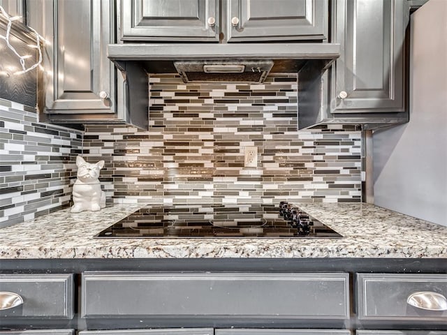 kitchen featuring backsplash, light stone countertops, black stovetop, and ventilation hood