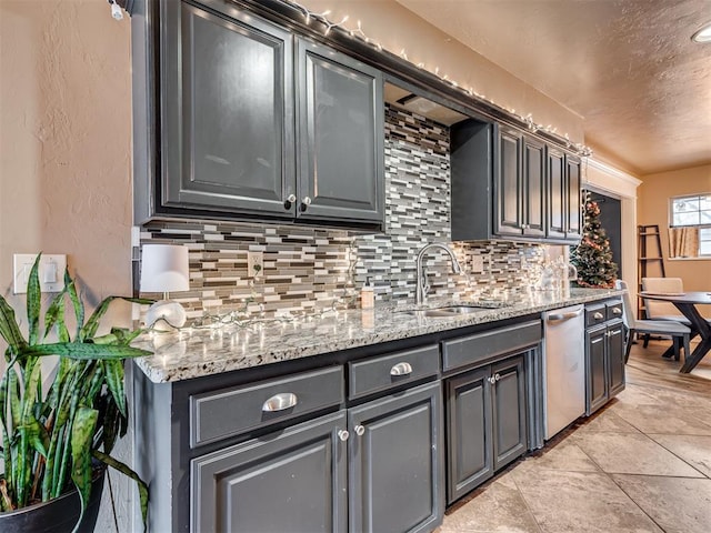 kitchen featuring tasteful backsplash, light stone counters, dishwasher, and sink