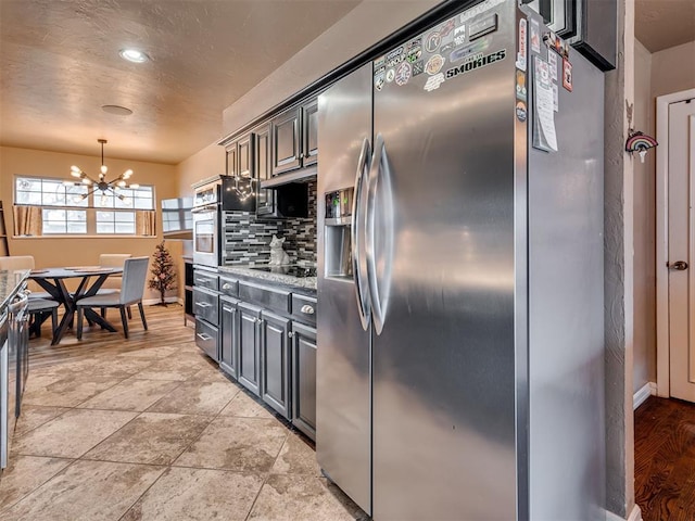 kitchen featuring backsplash, oven, stainless steel refrigerator with ice dispenser, black electric cooktop, and a notable chandelier