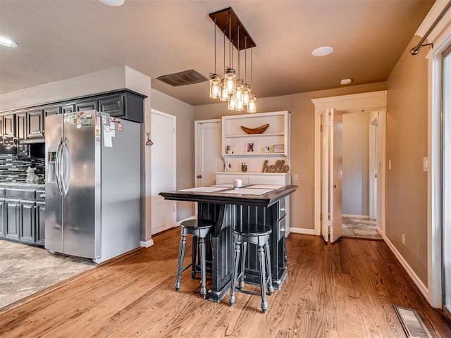 kitchen with gray cabinetry, a kitchen breakfast bar, hanging light fixtures, hardwood / wood-style flooring, and stainless steel fridge