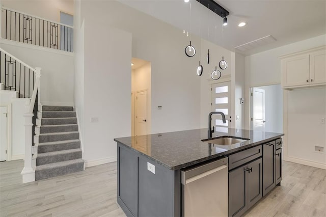 kitchen with dark stone counters, sink, stainless steel dishwasher, light wood-type flooring, and an island with sink