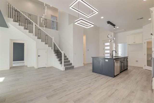 kitchen featuring white cabinetry, sink, light hardwood / wood-style flooring, stainless steel dishwasher, and a kitchen island with sink