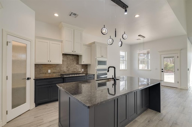 kitchen with appliances with stainless steel finishes, sink, a center island with sink, white cabinetry, and hanging light fixtures