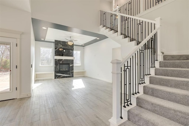 stairs with a fireplace, a wealth of natural light, a raised ceiling, and ceiling fan