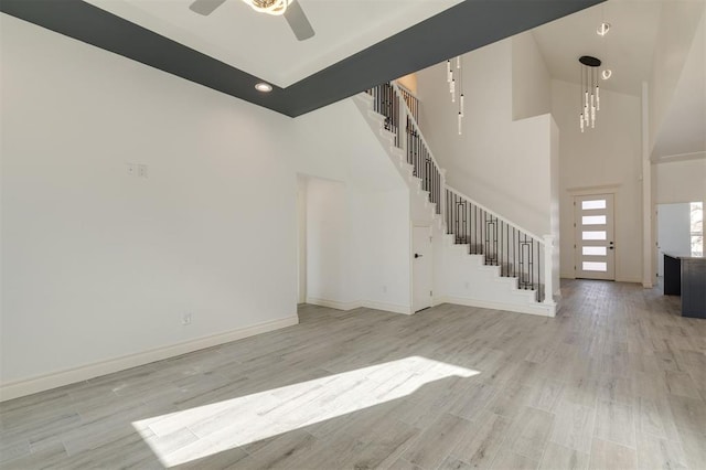 unfurnished living room with a towering ceiling, light hardwood / wood-style floors, and ceiling fan