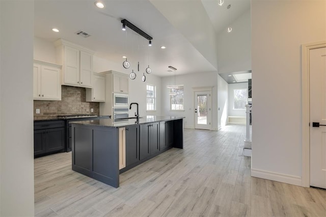 kitchen featuring built in microwave, hanging light fixtures, light hardwood / wood-style flooring, a kitchen island with sink, and white cabinets