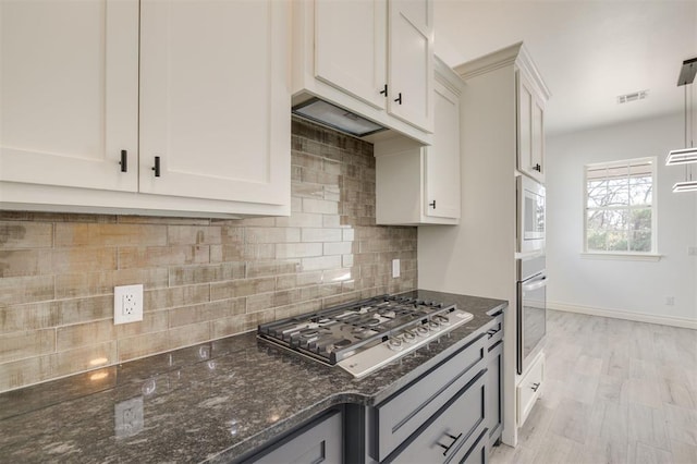 kitchen featuring white cabinets, decorative backsplash, dark stone countertops, and stainless steel appliances