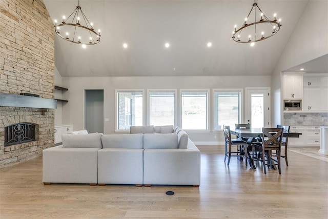 living room with high vaulted ceiling, a stone fireplace, and light hardwood / wood-style floors