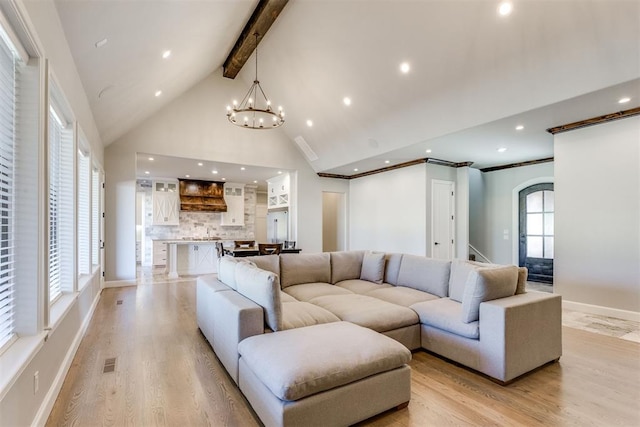 living room featuring an inviting chandelier, beamed ceiling, a healthy amount of sunlight, and light wood-type flooring