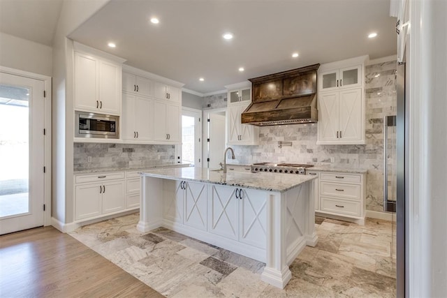 kitchen featuring a breakfast bar, a kitchen island with sink, appliances with stainless steel finishes, light stone counters, and white cabinetry