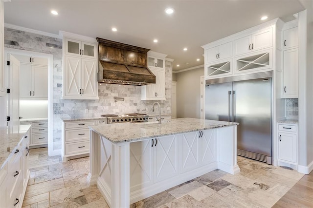 kitchen featuring sink, a kitchen breakfast bar, built in fridge, a center island with sink, and white cabinets