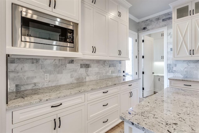 kitchen featuring white cabinets, decorative backsplash, stainless steel microwave, and ornamental molding