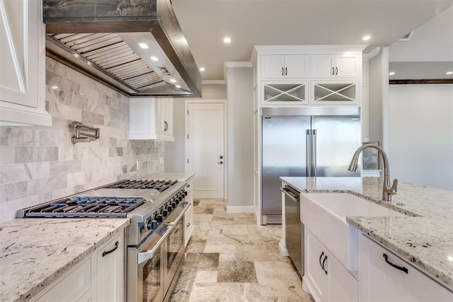 kitchen with light stone countertops, high end appliances, crown molding, wall chimney range hood, and white cabinets