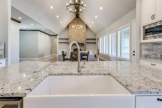 kitchen featuring white cabinetry, sink, stainless steel microwave, tasteful backsplash, and light stone counters