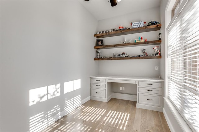 unfurnished office with ceiling fan, light wood-type flooring, and built in desk