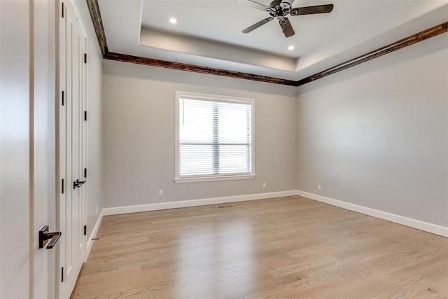 empty room with a tray ceiling, light hardwood / wood-style flooring, ceiling fan, and crown molding