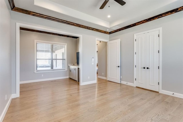 unfurnished bedroom featuring ceiling fan, a raised ceiling, light wood-type flooring, and crown molding