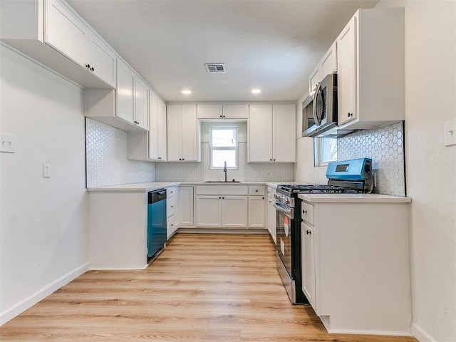 kitchen featuring appliances with stainless steel finishes, light wood-type flooring, sink, white cabinetry, and tasteful backsplash