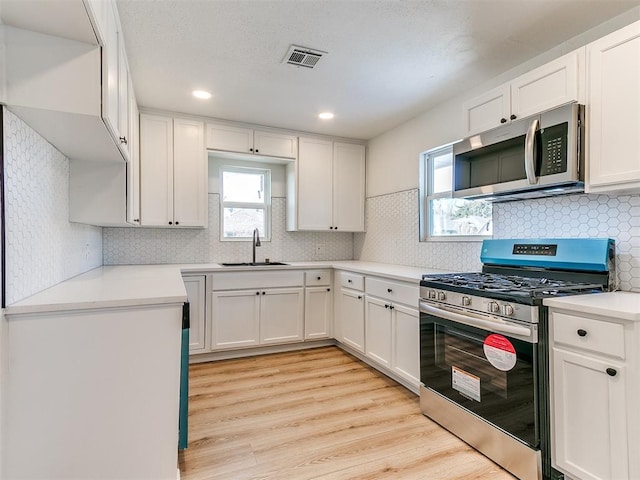 kitchen featuring appliances with stainless steel finishes, light wood-type flooring, sink, white cabinetry, and backsplash