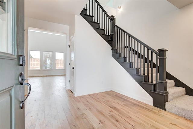 entryway featuring light wood-type flooring, a towering ceiling, and stairway