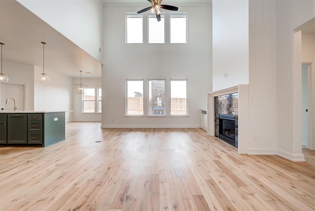 unfurnished living room with light wood finished floors, baseboards, a tiled fireplace, a ceiling fan, and a sink