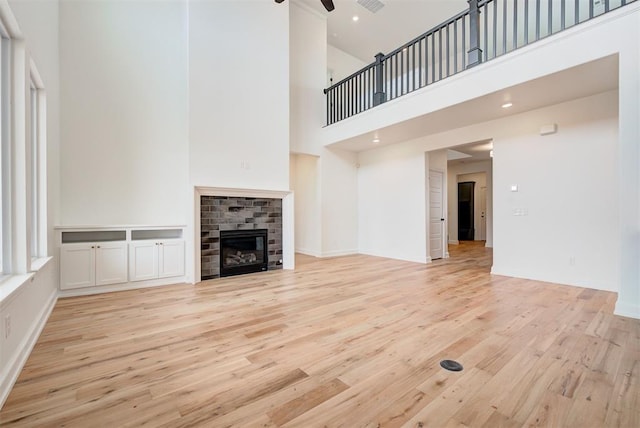 unfurnished living room with a glass covered fireplace, ceiling fan, a high ceiling, light wood-style floors, and recessed lighting