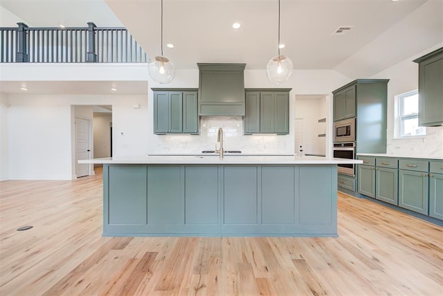 kitchen with light countertops, appliances with stainless steel finishes, a center island with sink, and pendant lighting