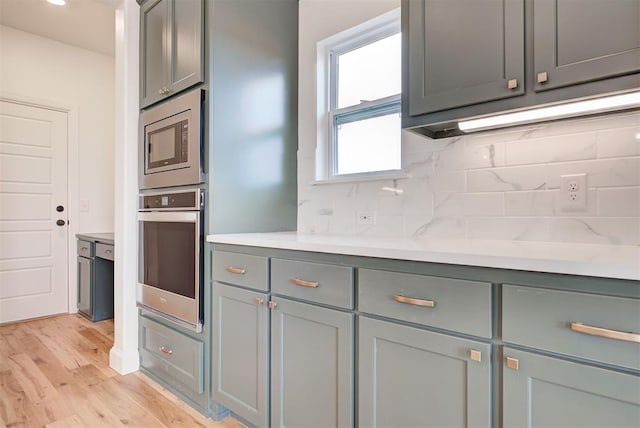 kitchen featuring light wood-style flooring, gray cabinetry, light countertops, appliances with stainless steel finishes, and decorative backsplash