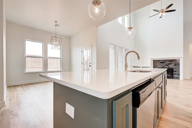 kitchen with light countertops, hanging light fixtures, a sink, an island with sink, and dishwasher