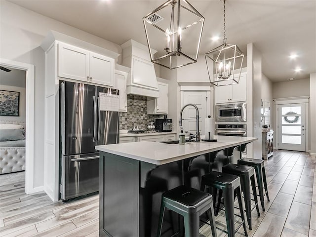 kitchen with stainless steel appliances, a kitchen breakfast bar, tasteful backsplash, a center island with sink, and white cabinets