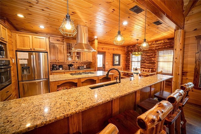 kitchen featuring appliances with stainless steel finishes, ventilation hood, sink, log walls, and decorative light fixtures