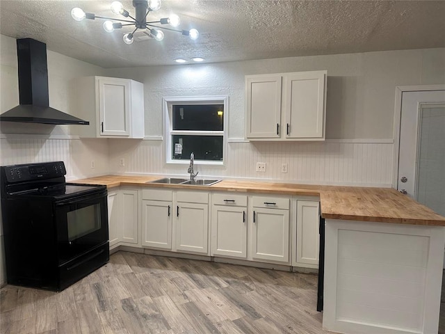 kitchen with wall chimney exhaust hood, sink, butcher block countertops, white cabinetry, and black / electric stove