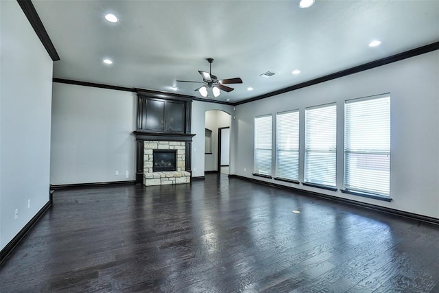 unfurnished living room with a stone fireplace, crown molding, ceiling fan, and dark hardwood / wood-style floors