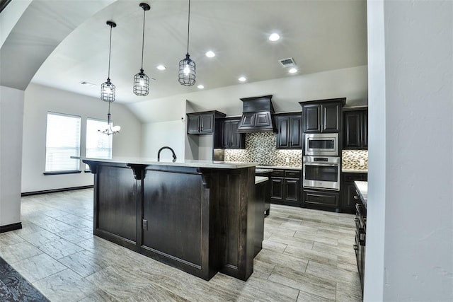 kitchen featuring custom exhaust hood, a breakfast bar, stainless steel appliances, hanging light fixtures, and an island with sink