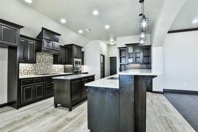 kitchen featuring a kitchen island with sink, sink, stainless steel appliances, and decorative light fixtures