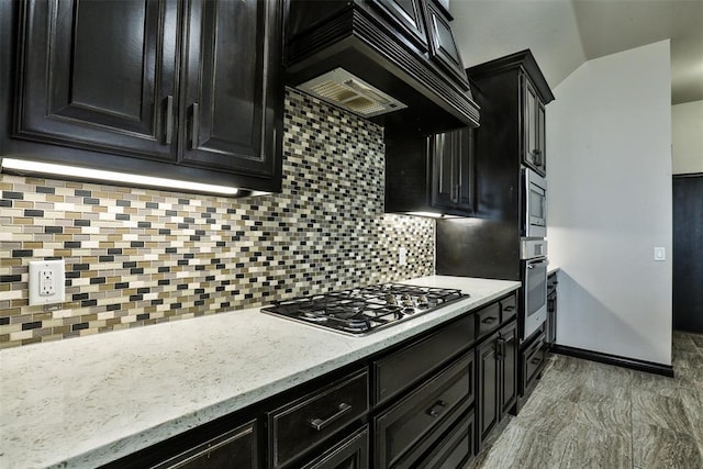 kitchen featuring custom exhaust hood, light stone counters, decorative backsplash, and appliances with stainless steel finishes