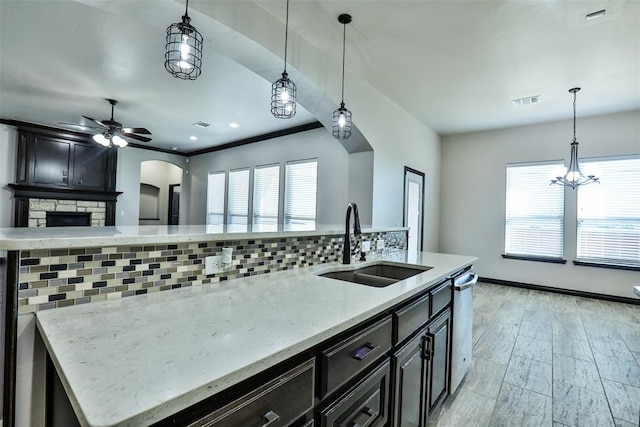 kitchen with dishwasher, backsplash, a center island with sink, sink, and hanging light fixtures