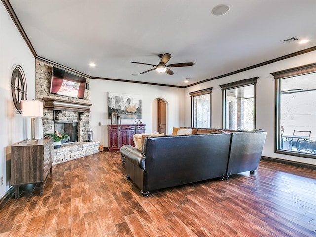 living room featuring dark hardwood / wood-style flooring, ceiling fan, a stone fireplace, and crown molding