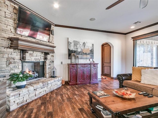 living room featuring crown molding, a stone fireplace, and dark wood-type flooring