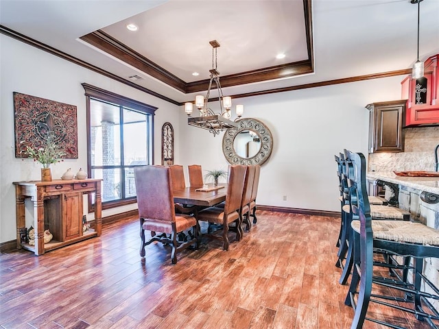 dining room featuring light wood-type flooring, a raised ceiling, and crown molding