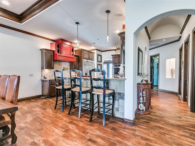 kitchen with dark wood-type flooring, crown molding, tasteful backsplash, a kitchen bar, and stainless steel appliances