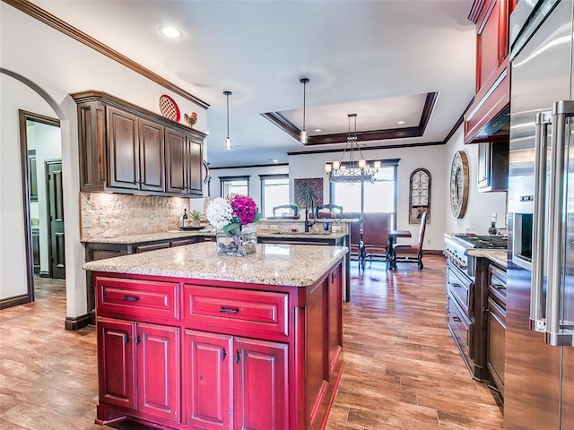 kitchen featuring a notable chandelier, pendant lighting, a tray ceiling, high quality appliances, and a kitchen island